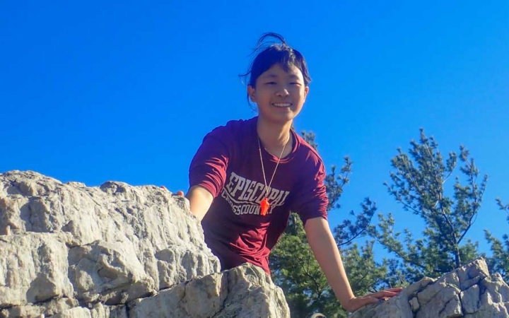 a girl on a rock smiles down at the camera on a backpacking course